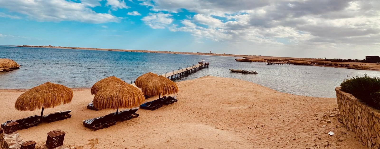 Straw umbrellas on the beach at Sharm El Naga with the wooden pier reaching into the bay